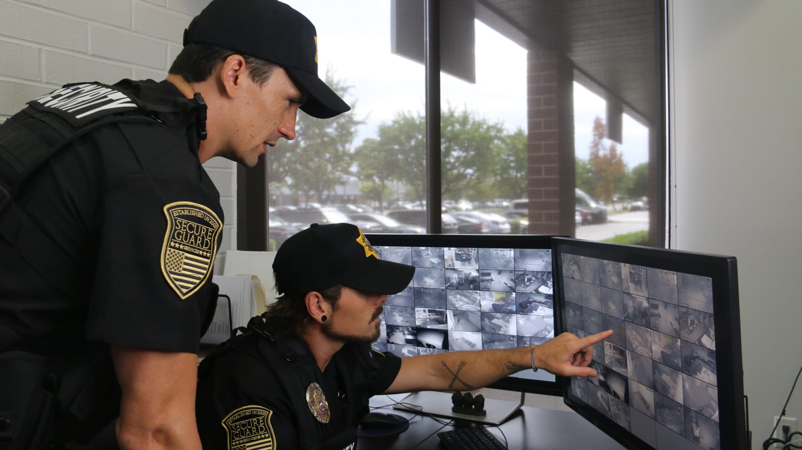 Two professional security guards monitoring surveillance cameras in a control room, ensuring 24/7 property protection.