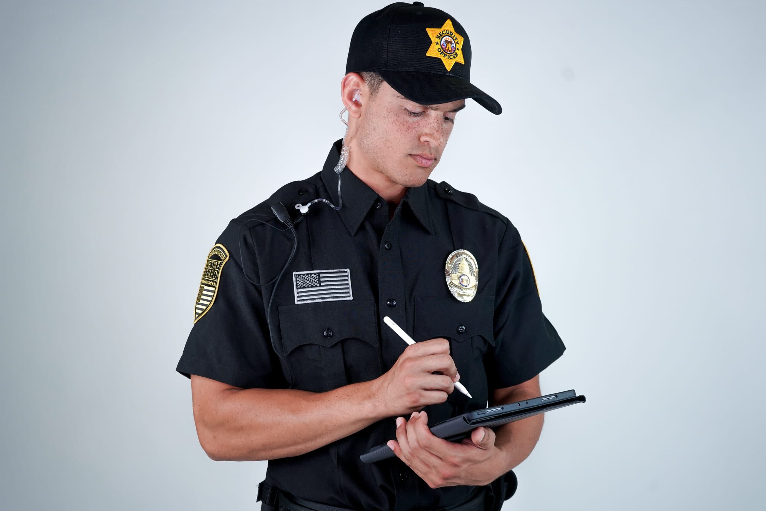 A security consultant assessing a building's access points while reviewing a checklist, with surveillance cameras and fencing in the background.