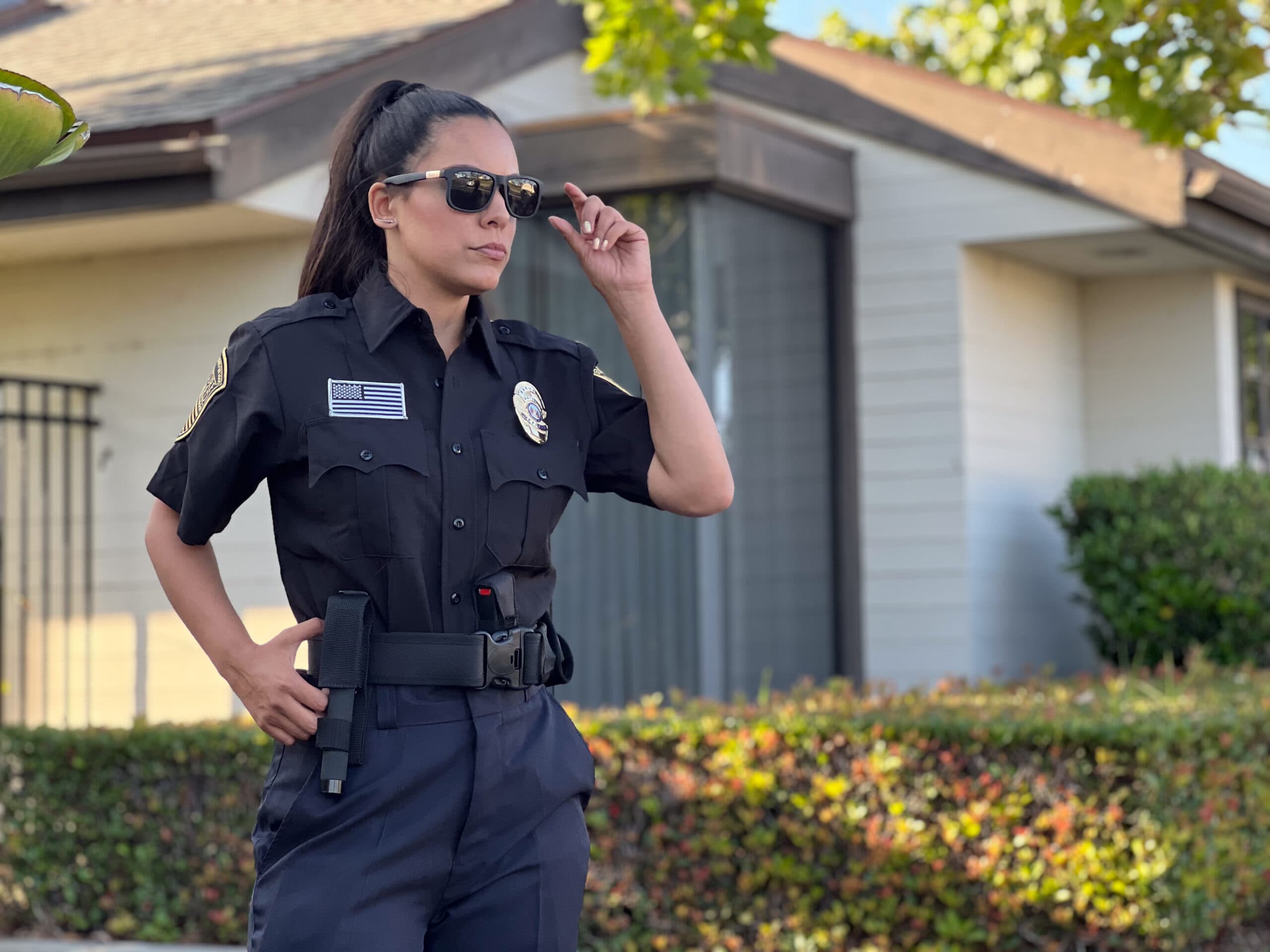 A uniformed security officer wearing sunglasses stands outdoors in front of a residential property, maintaining a professional and alert presence.