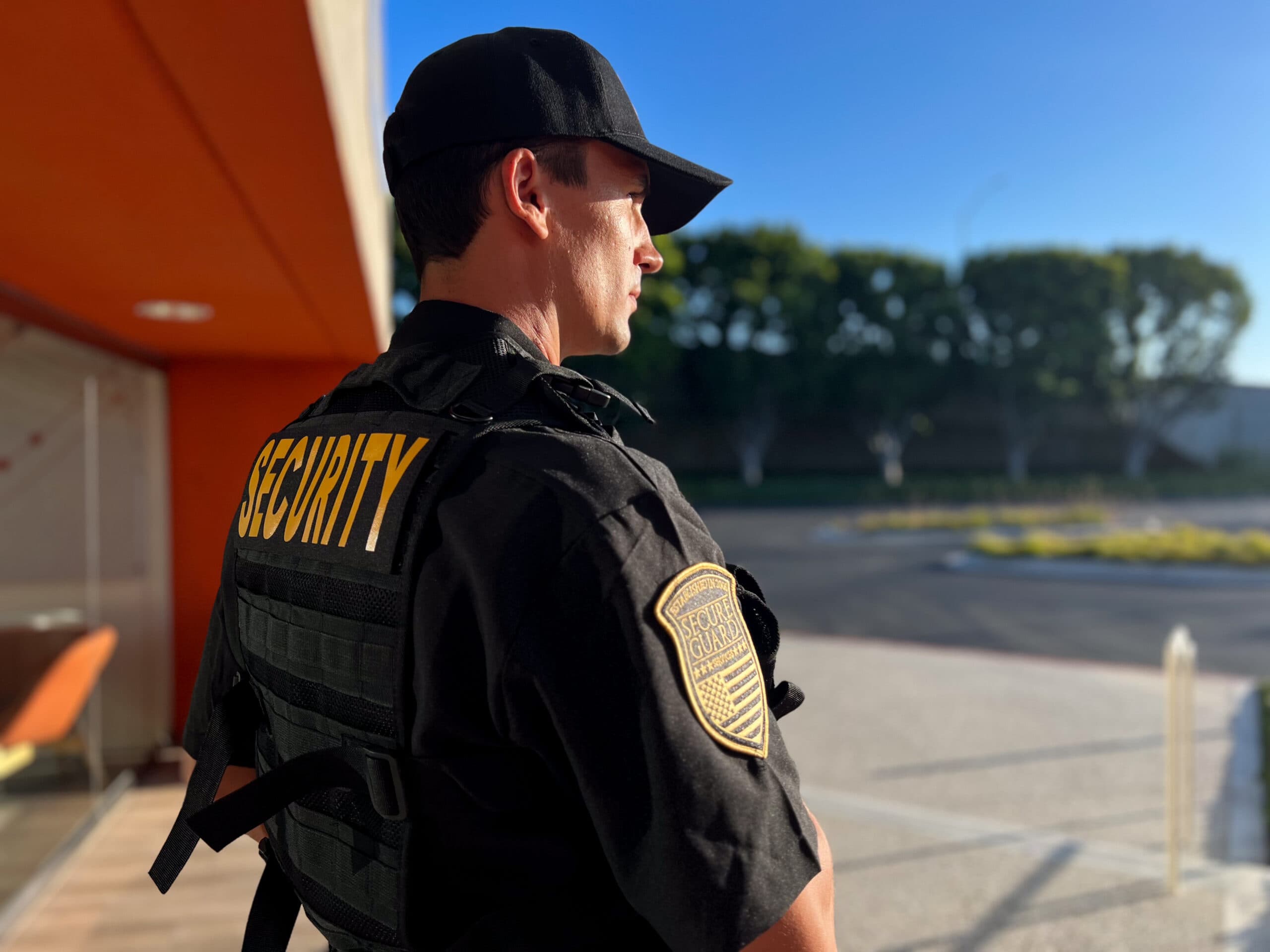 Security guard standing alert outside a commercial building, providing professional workplace protection during daylight hours.