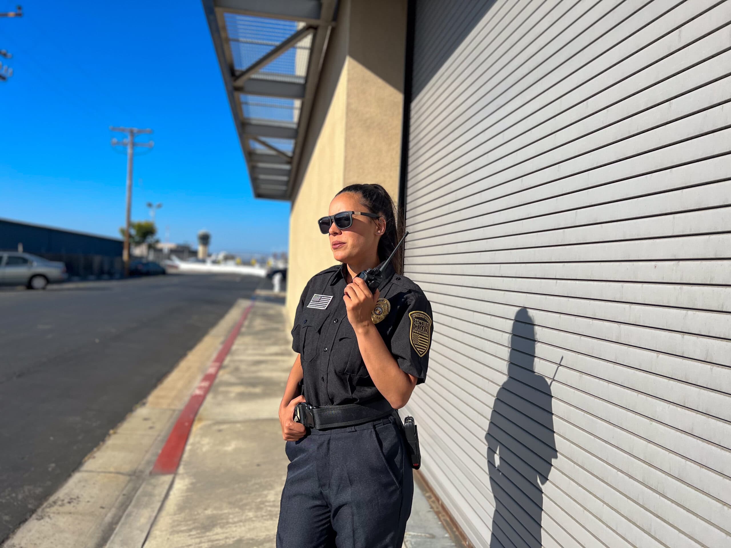 Professional Fresno security guard standing on patrol outside a commercial property, using a radio to monitor safety and protect businesses and facilities.