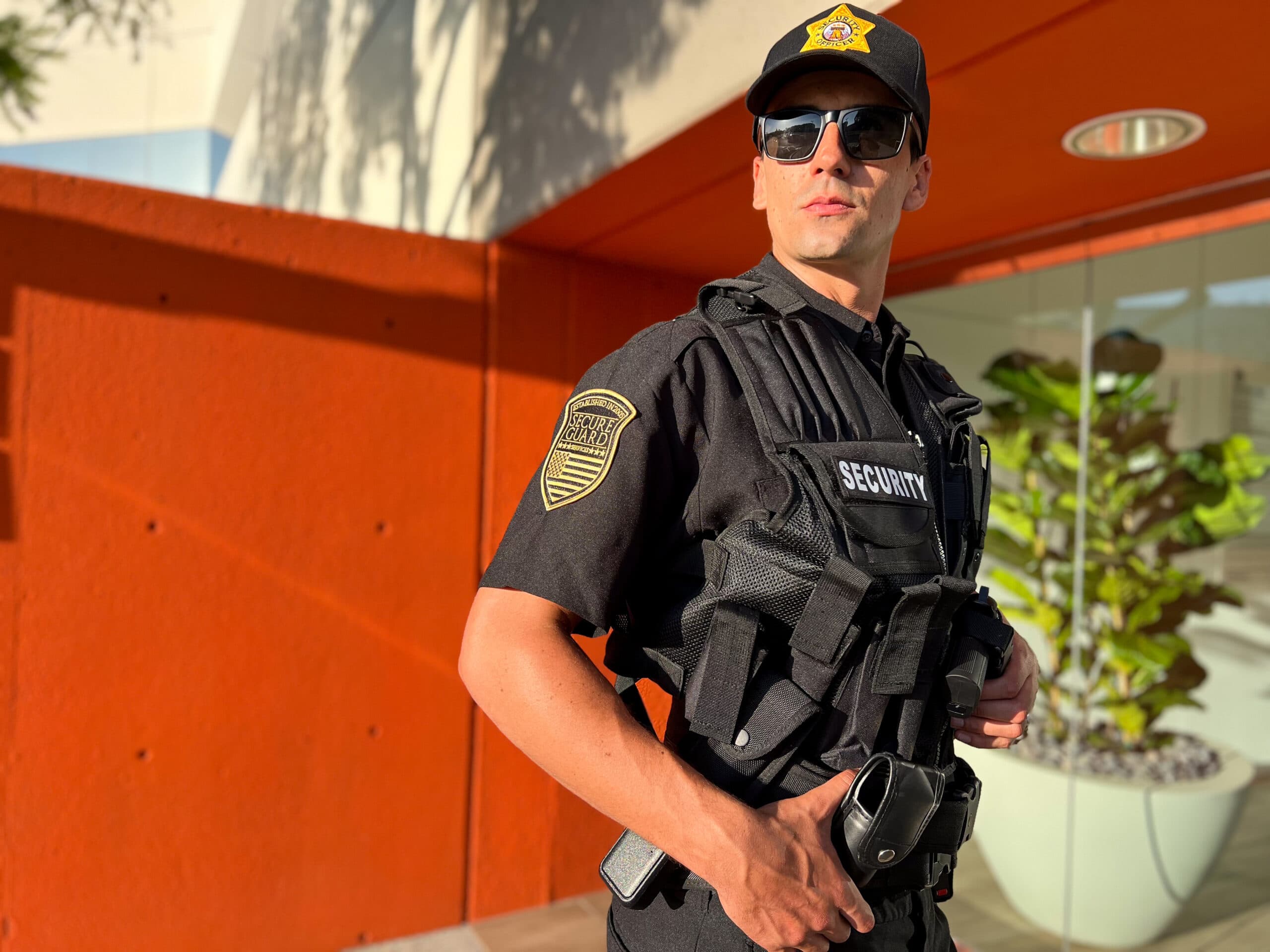 Professional security guard in tactical uniform standing alert outside a commercial building, demonstrating proactive security presence and risk prevention